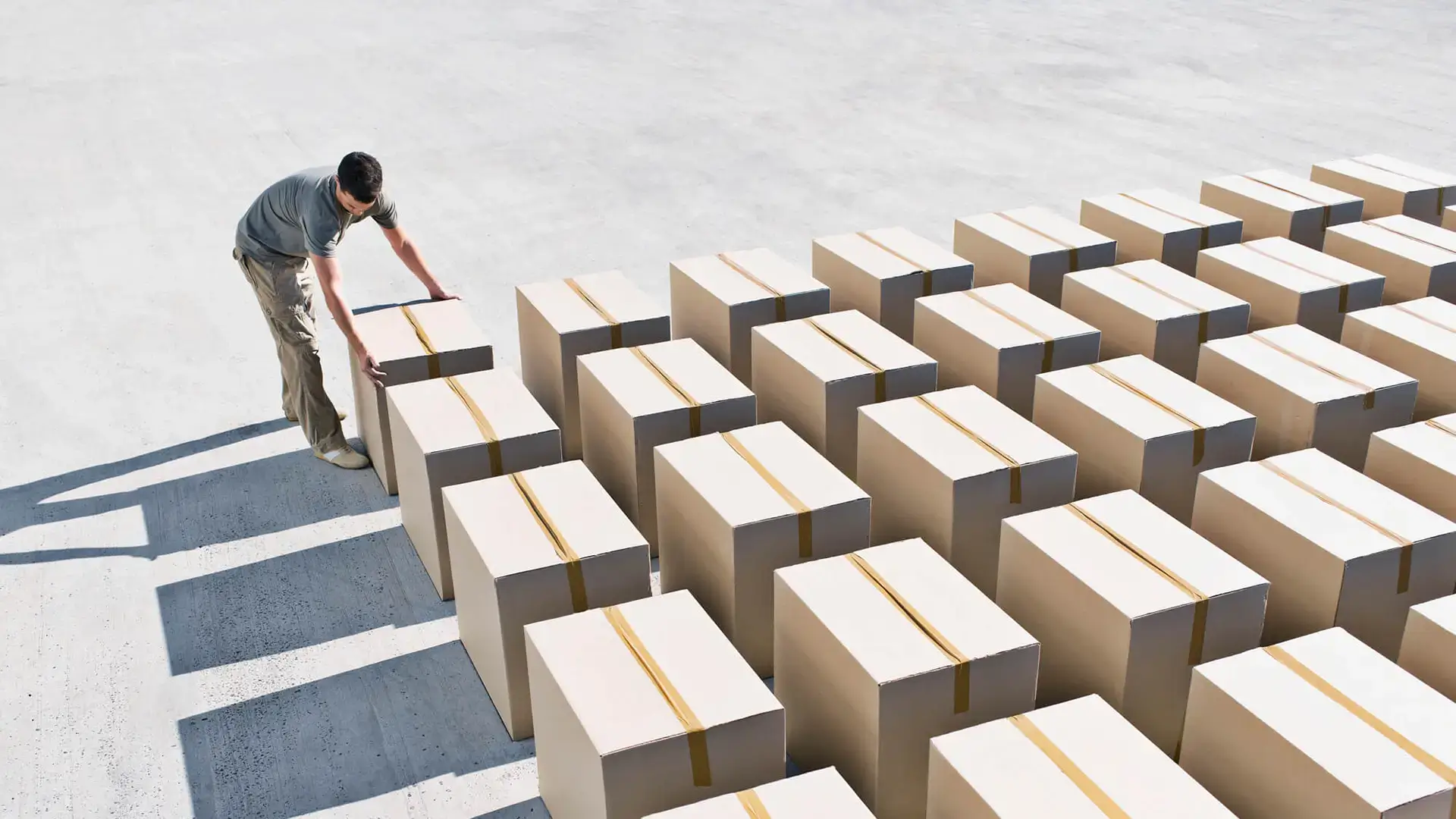 A man in the sun laying out unifom cardboard boxes in rows