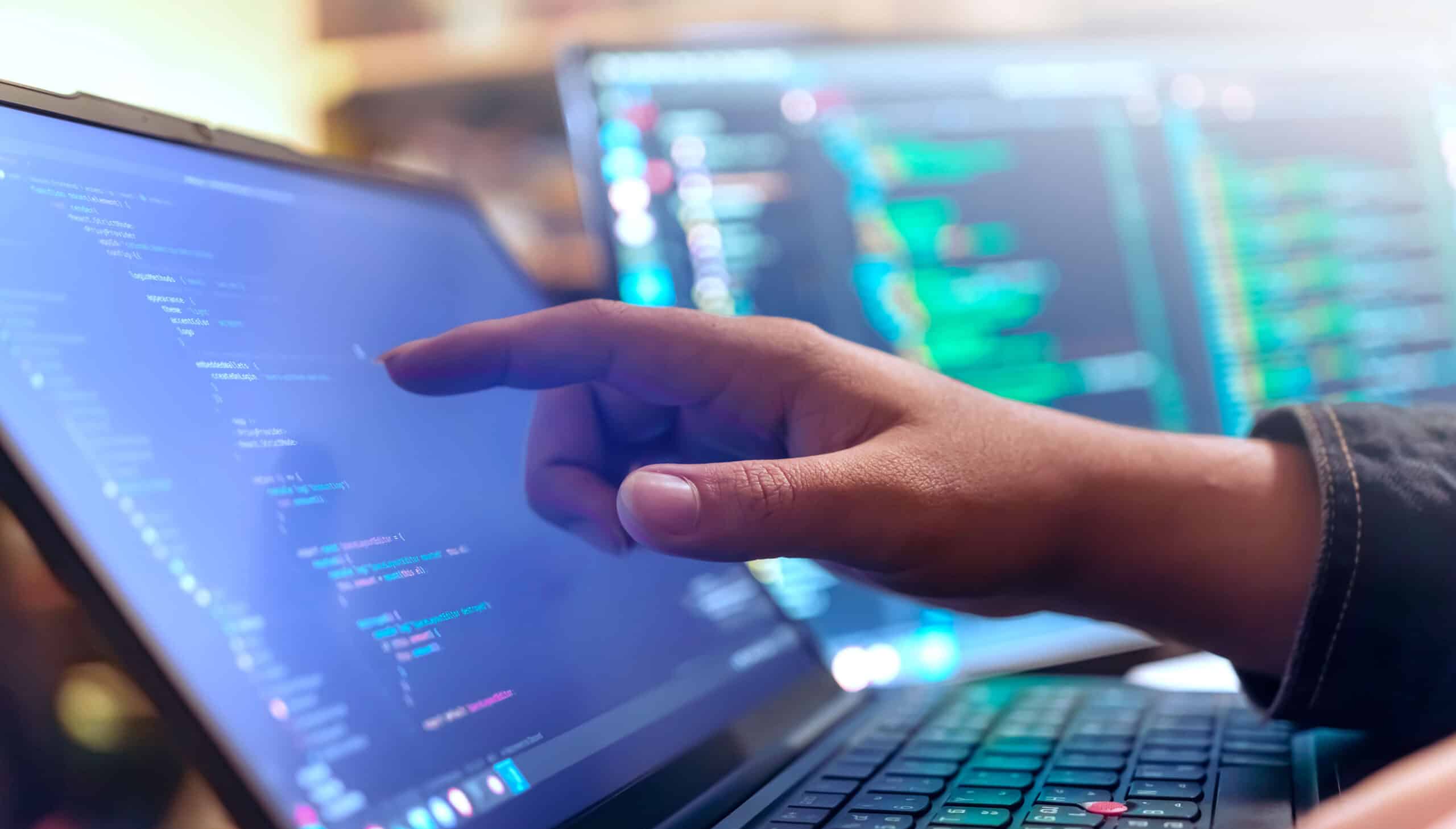 A person's finger pointing to a line of code on an open laptop
